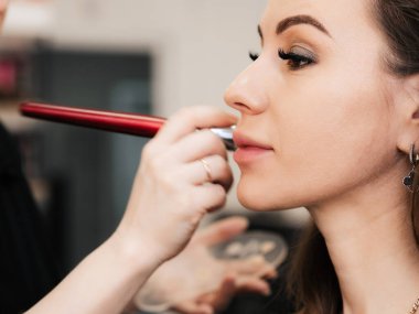 Makyaj sanatçılarının eli gölgeli bir fırçayla bir kadının yüzüne makyaj yapıyor.