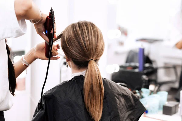 Kadeřník dělá ocas účes pro ženu s dlouhými hnědými vlasy — Stock fotografie