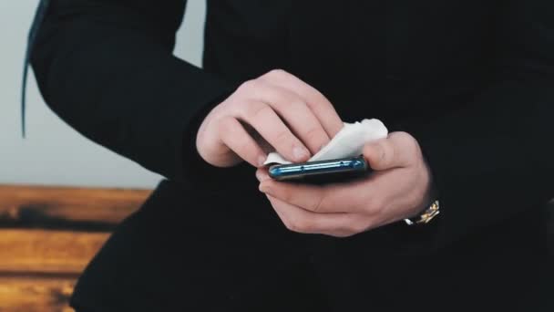 Концепция коронавирусной эпидемии COVID-19. Мужчина вытирает экран смартфона мобильного телефона влажной салфеткой — стоковое видео