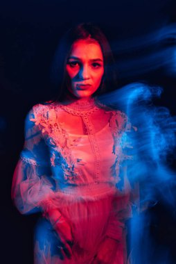 Karanlık bir arka planda elbise giymiş endişeli genç bir kızın portresi.