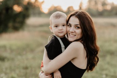 Genç beyaz anne yazın küçük oğluna sarılırken gülümsüyor.