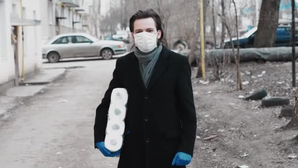 Человек в медицинской маске и перчатках для защиты от эпидемии коронавируса с рулонами туалетной бумаги — стоковое видео
