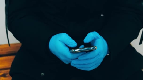 Hände eines Mannes in Handschuhen zum Schutz vor dem Coronavirus COVID-19 mit einem Mobiltelefon — Stockvideo
