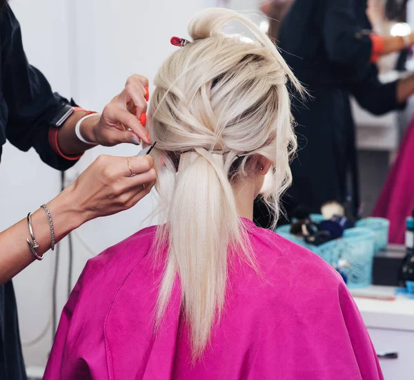 Mãos de um cabeleireiro profissional fazer um penteado para uma menina loira com cabelo longo — Fotografia de Stock