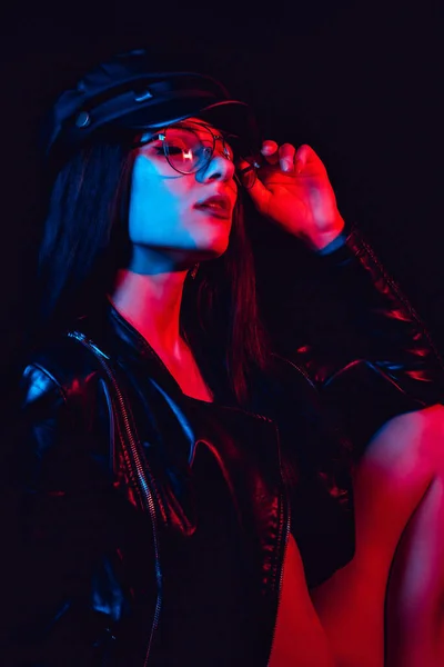 Fashion portrait of a sexy girl with glasses in a leather jacket and cap — Stock Photo, Image