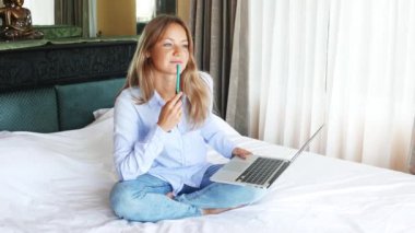 Yatak odasında dizüstü bilgisayarda çalışan güzel beyaz kadın. MacBook kullanarak ve gülümseyen genç tatlı kız. Güzel mutlu teen yatakta oturma ve sınavları için hazırlanıyor. Güneşli sabah.