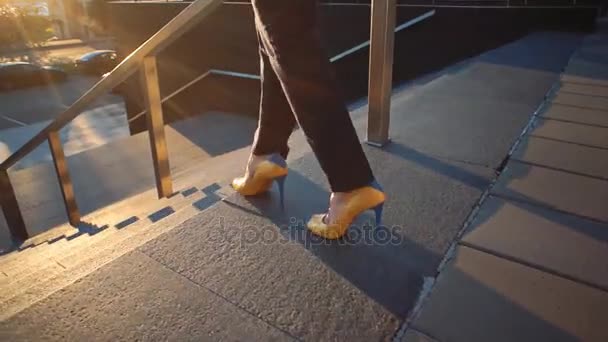 Όμορφη κοπέλα με ένα κίτρινο παπούτσια για Γεια σας τακούνια που έρχονται κάτω από τις σκάλες. Κινηματογραφικό στυλ βίντεο. Δείτε στα πόδια και τα παπούτσια κίτρινο-μπλε. — Αρχείο Βίντεο