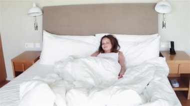 Genç kadın yatakta iyi uykudan sonra kalkıp rahat yuvasına, terk etmeye isteksiz oturan kollarını outstretching bir gün mutlu ve rahat, verimli çalışması için hazır giriyoruz. Arkadan görünüş