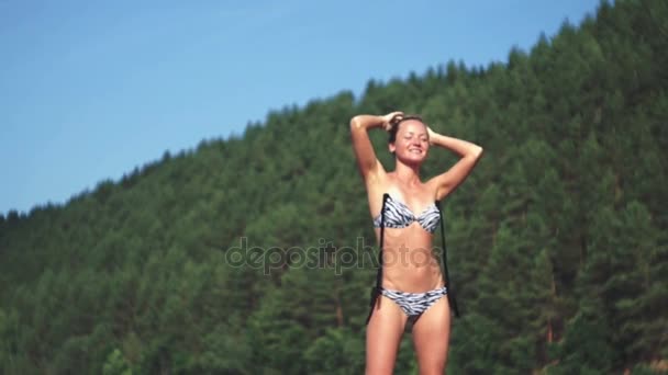 Tiro ao ar livre de sorrir jovem modelo feminino em biquíni dançando contra o céu azul e floresta verde. Mulher se divertindo em um dia de verão . — Vídeo de Stock