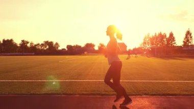 Oyundaki bir banliyösünde, sağlıklı fitness sağlık canlılık atlet karşı güneş patlaması kontrast çalıştıran. Stadyumda günbatımında çalışan genç kadın