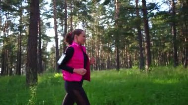 Spor kıyafetleri giyen ve baharda dağdaki yeşil ormanda koşan güzel bir kız.