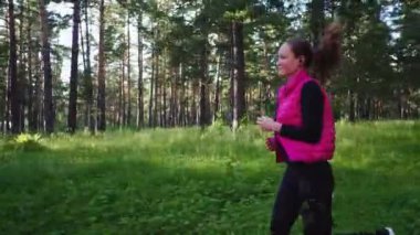 Spor kıyafetleri giyen ve baharda dağdaki yeşil ormanda koşan güzel bir kız.