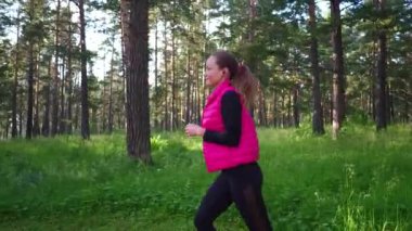 Spor kıyafetleri giyen ve baharda dağdaki yeşil ormanda koşan güzel bir kız.