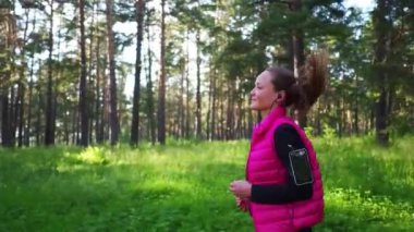 Spor kıyafetleri giyen ve baharda dağdaki yeşil ormanda koşan güzel bir kız.