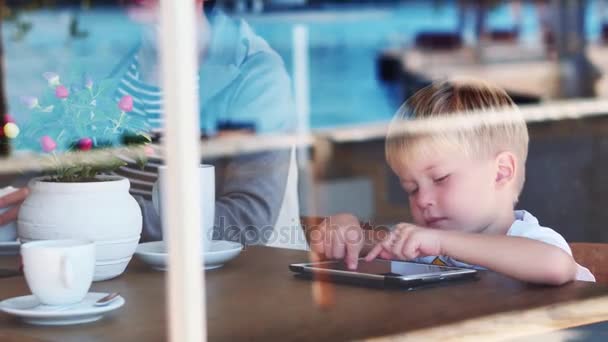 4 roky starý děti chlapce, který seděl na dřevěné desce při hraní s zařízení pad tablet na city café — Stock video