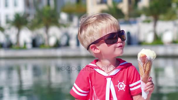 Крупним планом маленький хлопчик з сонцезахисними окулярами їсть морозиво на пристані — стокове відео