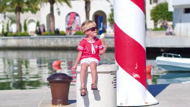 Крупный план маленького мальчика в солнечных очках, поедающего мороженое на пристани — стоковое видео