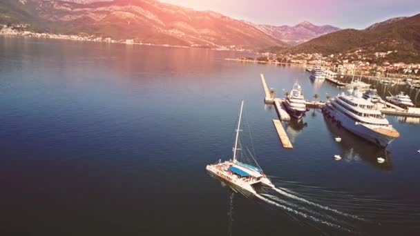 Vista aérea de barcos y hermosa arquitectura al atardecer en Europa. Paisaje colorido con barcos en la bahía marina, mar, ciudad, montañas. Vista superior desde el dron del puerto con yate y velero — Vídeo de stock