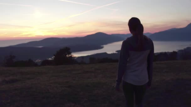 Gün batımında dağ tepe üzerinde yürüyen genç kadın — Stok video