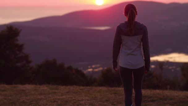 Mladá žena procházky při západu slunce na vrchol hory — Stock video