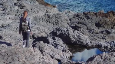 Genç kadın hiker cliff üzerinde duran ve deniz, gökyüzü arka plan üzerinde dört gözle sırt çantası ile. Bayan turist manzarayı bir dağın zirvesinde.