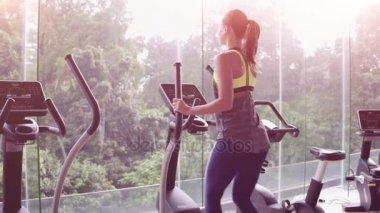 Yakın çekim. Arkadan görünüşü çekici genç kadın spor salonunda eliptik bir eğitmen olarak çalışma dışarı. Panoramik pencerelere