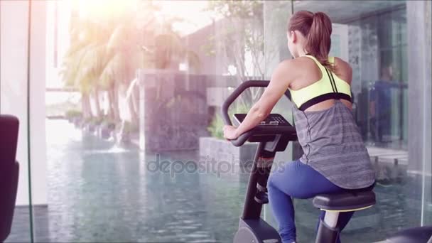 Vista trasera de la atractiva mujer en el gimnasio montando en la bicicleta giratoria con una enorme ventana panorámica — Vídeos de Stock