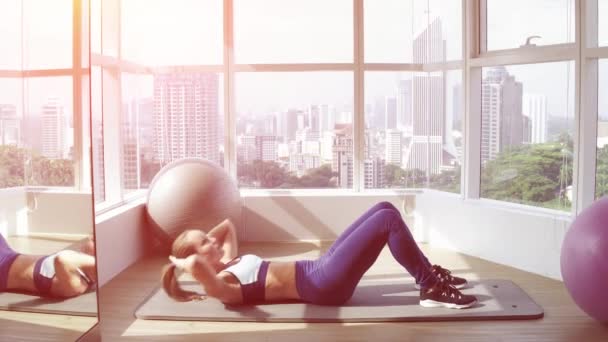 年轻的健身妇女做仰卧起坐附近的全景窗口在健身房。早晨和太阳升起. — 图库视频影像