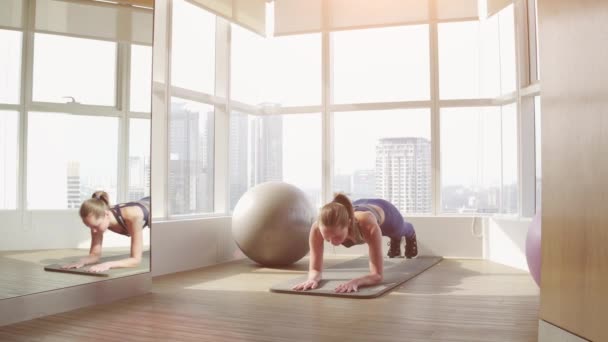 Un tablón perfecto. Vista lateral de larga duración de la joven hermosa mujer en ropa deportiva haciendo tablón mientras está de pie frente a la ventana en el gimnasio — Vídeos de Stock