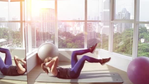 Jonge fitness vrouw doen crunches oefeningen in de buurt van een panoramisch venster op de sportschool. 'S morgens en zon opkomst. — Stockvideo