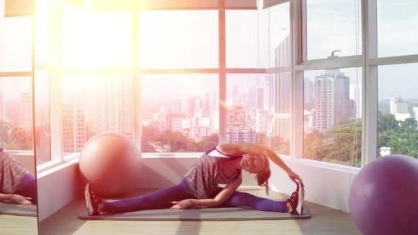 Grandi progressi. Giovane bella donna in abbigliamento sportivo facendo stretching mentre seduto sul pavimento di fronte alla finestra in palestra. Luminoso sole splendente . — Video Stock