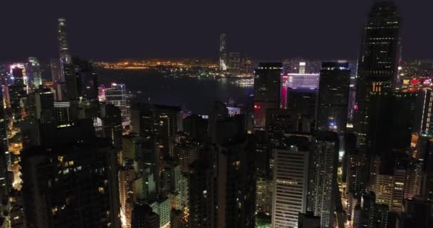 AERIAL. Victoria Harbor vista con horizonte de Hong Kong y rascacielos urbanos por la noche . — Vídeos de Stock