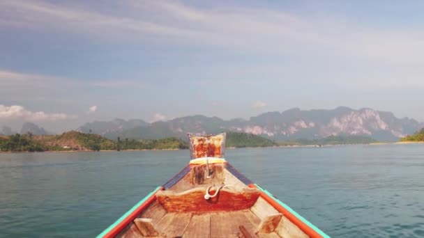 Wooden Thai traditional long-tail boat on a lake with mountains and rain forest in the background during a sunny day at Ratchaprapha Dam at Khao Sok National Park, Surat Thani Province, Thailand — Stok Video