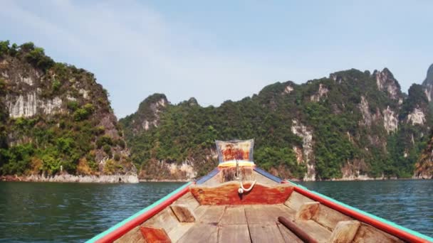 Wooden Thai traditional long-tail boat on a lake with mountains and rain forest in the background during a sunny day at Ratchaprapha Dam at Khao Sok National Park, Surat Thani Province, Thailand — Stok Video