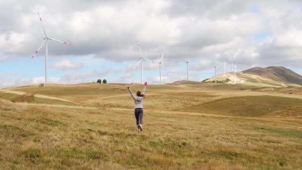 Femme est tombée les mains libres et levantes. Turbines éoliennes sur fond de coucher de soleil. Production d'énergies renouvelables alternatives 