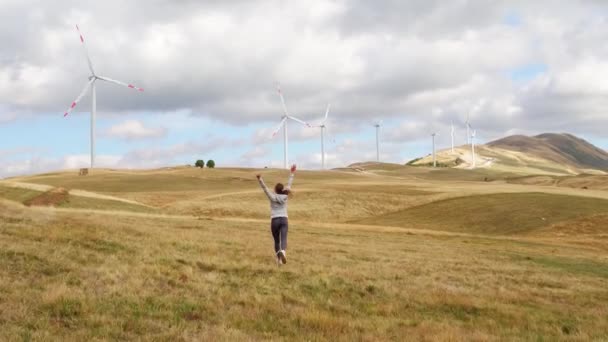 Femeia a căzut liberă şi a ridicat mâinile. Turbine eoliene pe fundalul apusului de soare. Producția alternativă de energie regenerabilă — Videoclip de stoc