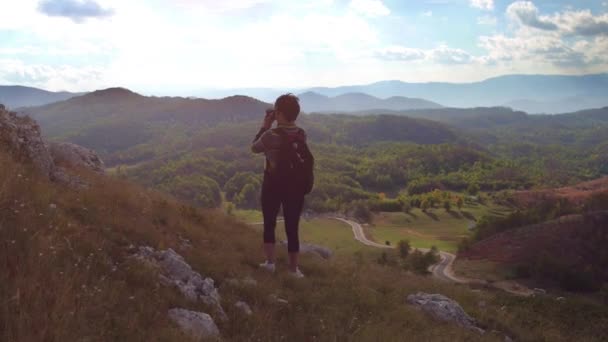 Молодая женщина фотограф делает фото на вершине горы при сильном ветре — стоковое видео