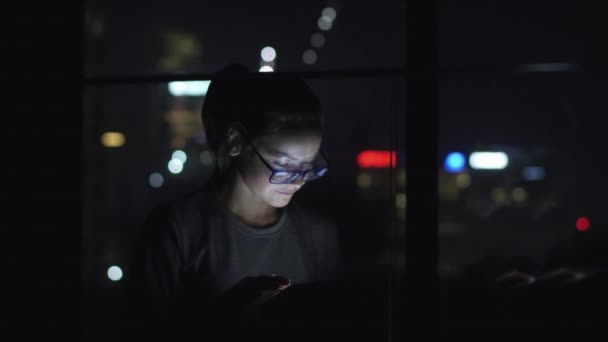 Mujer en gafas usando la tableta pc y sentada al lado de la ventana. Bokeh en el fondo — Vídeo de stock