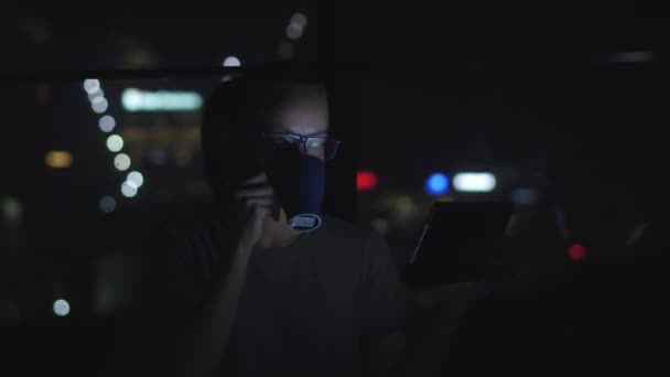 Nő a szemüveg segítségével a tábla-pc és a teaivás az ablak mellett éjjel. A háttérben a bokeh — Stock videók