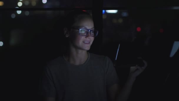 Szemüveges nő beszél a táblagép mellett videokonferencia az ablak mellett. Bokeh a háttérben — Stock videók