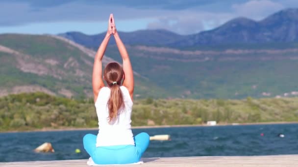 Bliska - widok z tyłu z kobieta robi ćwiczenia jogi na plaży z morzem i górami w tle. Wiatr i fala splash. — Wideo stockowe