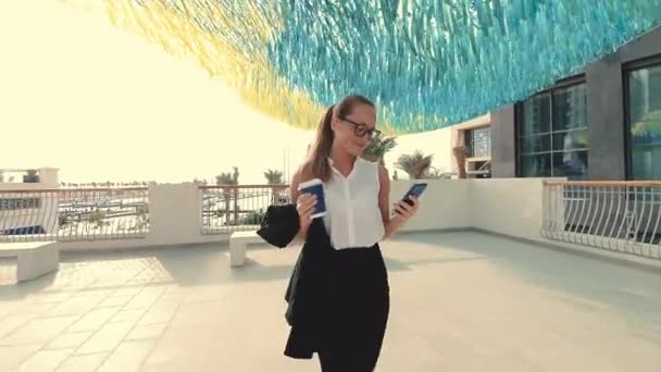Ευτυχισμένη γυναίκα στέλνει μηνύματα στο smartphone. Εκτελεστική εργασία με ένα κινητό τηλέφωνο στο δρόμο με κτίρια γραφείων στο παρασκήνιο — Αρχείο Βίντεο