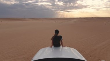 Genç gezgin kadın çölde arabada oturuyor. Seyahat kavramı.
