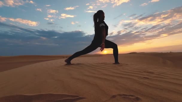 Dev çölde gün batımında yoga yapan genç bir kadının silueti. Destansı günbatımı ve spor konsepti videosu. — Stok video