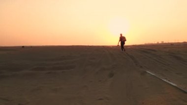 Sarı otantik sırt çantalı sarışın kadın kum fırtınasından sonra kumlu yola bakıyor. Çölde seyahat maceraları.