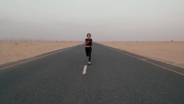 Joven mujer en forma corriendo en un camino en un desierto — Vídeos de Stock