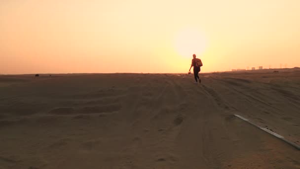 Back view blond hair woman with yellow authentic backpack looking on sandy road after sandstorm. Travel adventures in desert. — Stock Video