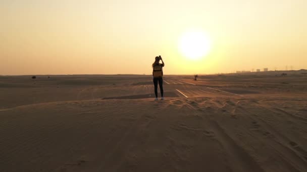 Vue de dos femme blonde cheveux avec sac à dos authentique jaune regardant sur la route sablonneuse après tempête de sable. Aventures de voyage dans le désert.