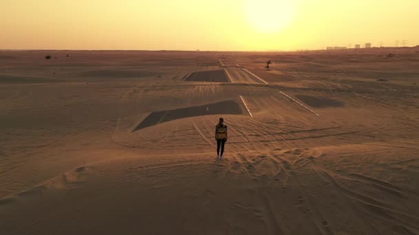 Vue de dos femme blonde cheveux avec sac à dos authentique jaune regardant sur la route sablonneuse après tempête de sable. Aventures de voyage dans le désert.