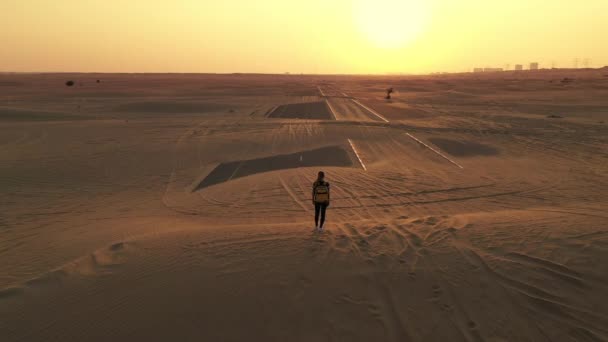 Bakåt visa blont hår kvinna med gul autentisk ryggsäck tittar på sandig väg efter sandstorm. Reseäventyr i öknen. — Stockvideo